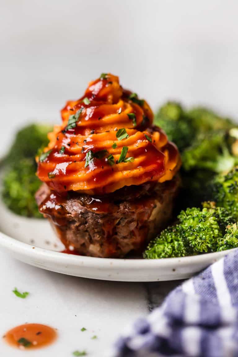 A BBQ meatloaf muffin with sweet potato topping next to broccoli. 