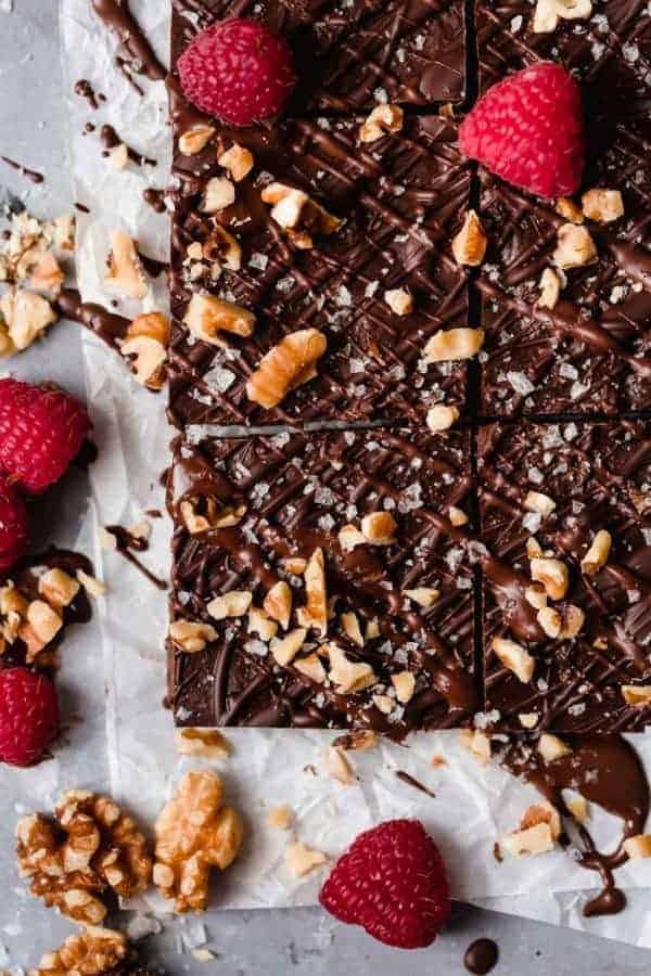Overhead photo of the Vegan No-Bake Brownies on a piece of white parchment with raspberries, walnuts and chocolate drizzle. 
