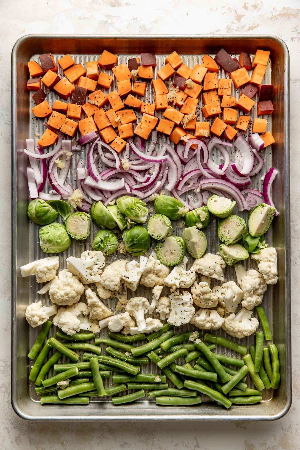 Sweet potatoes, red onions, Brussels sprouts, cauliflower, and green beans on a sheet pan.