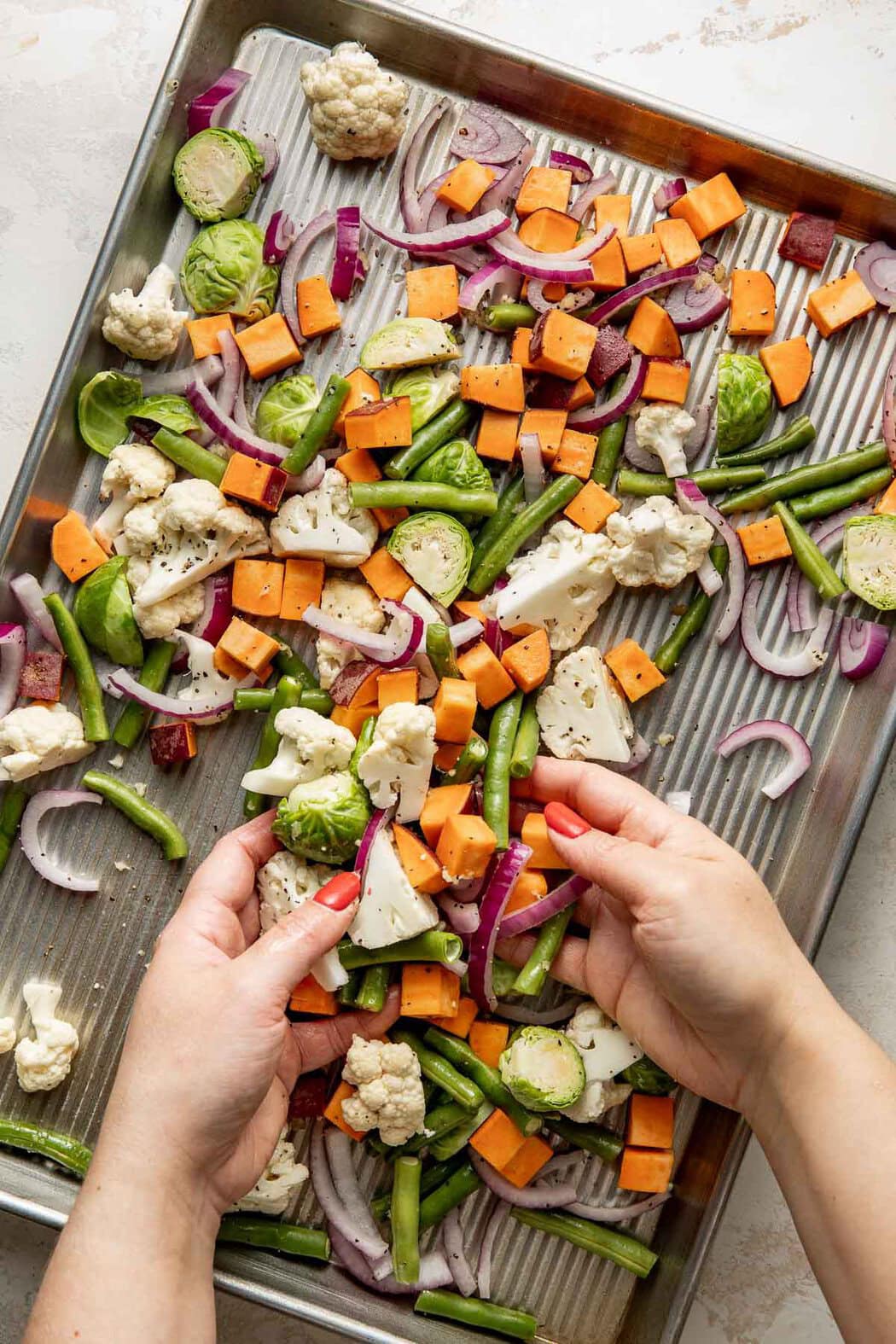 Two hands tossing raw vegetables on a sheet pan.