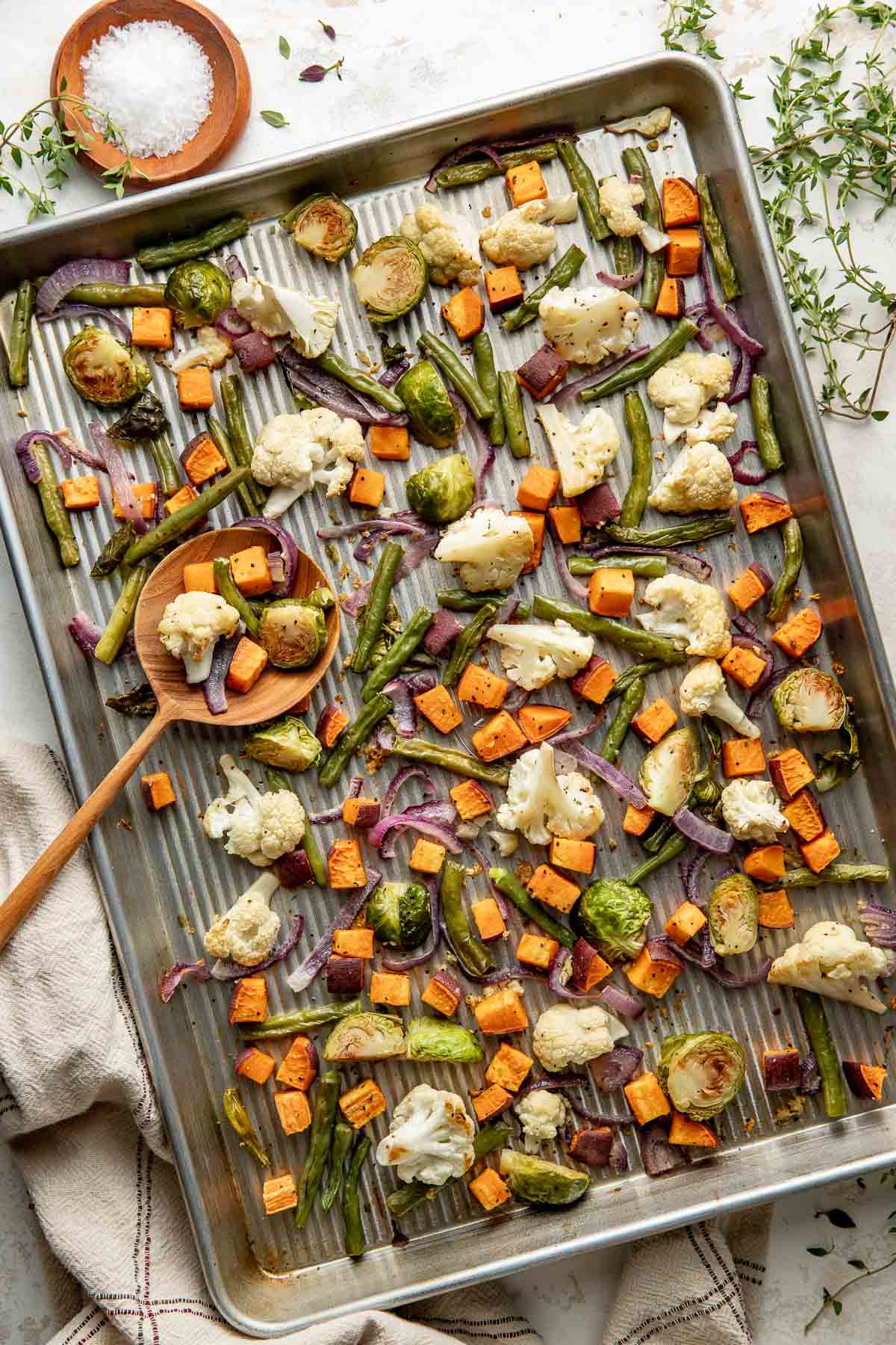 A sheet pan of roasted vegetables, a wooden spoon with a scoop.