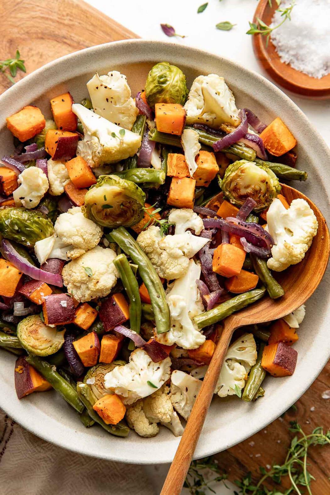 A bowl of roasted vegetables with a wooden spoon sticking out.