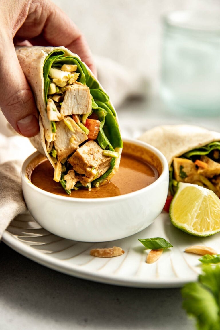 Close up view of an Asian-Inspired Chicken Salad wrap being dipped in a peanut sauce. 