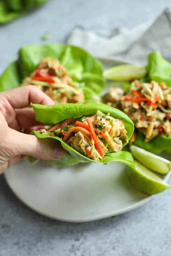 Asian Chicken Salad Lettuce Wraps on a white plate with one being picked up 