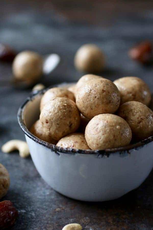 Straight on photo of Nutty Cashew Bites in a tea cup with cashews and dates surrounding. 