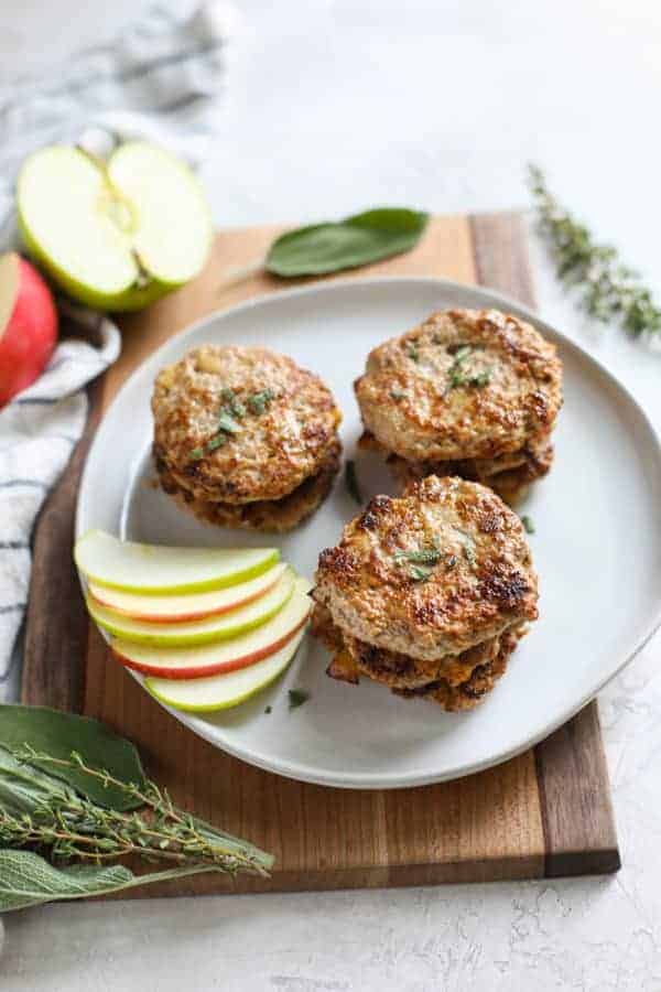 Turkey Apple Sausage Patties stacked by twos on a white plate with apple slices on the side