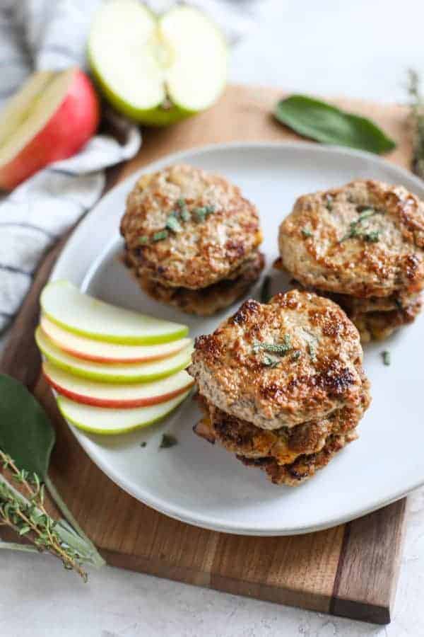 Turkey Apple Sausage Patties stacked on a white plate with a side of apple slices