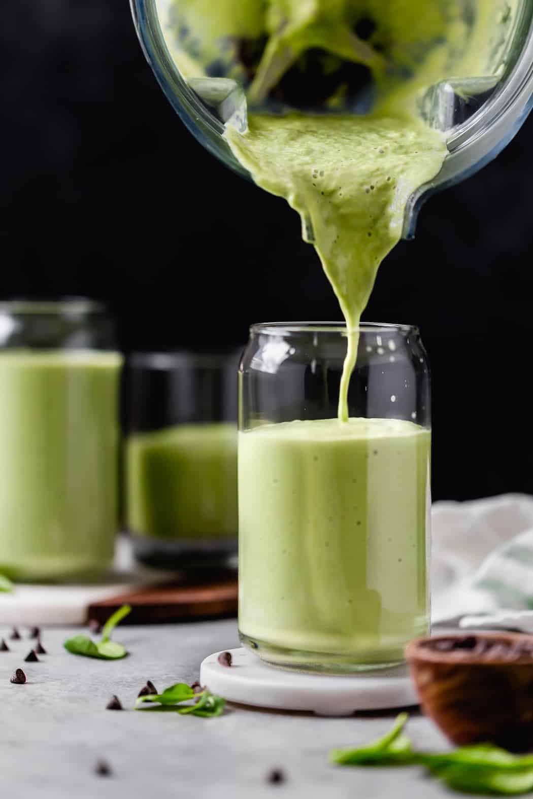 A green mint chocolate chip smoothie slowly being poured into glass cups
