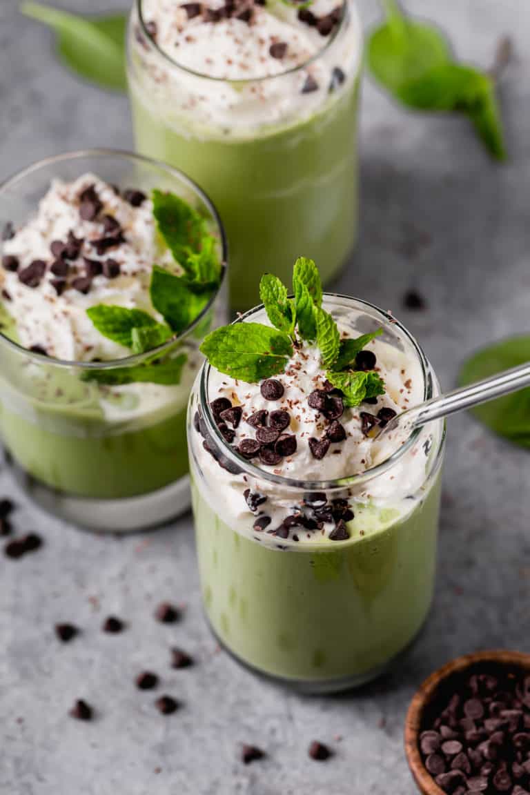 Overhead view of vibrant green mint chocolate chip milkshake topped with whipped cream, chocolate chips, and Mint leaves. 
