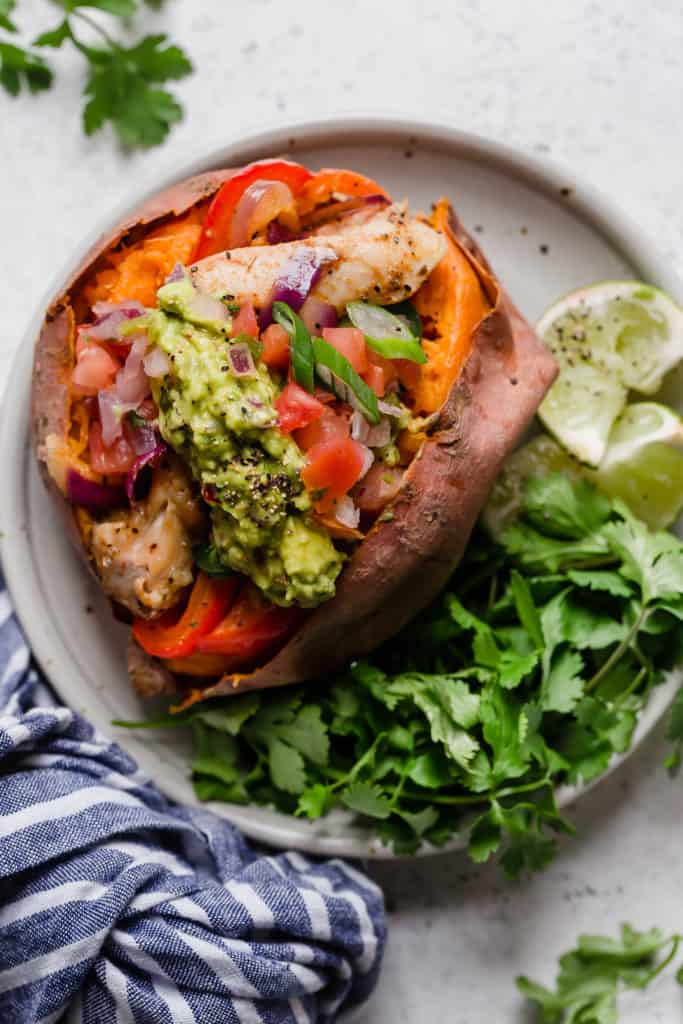 Chicken fajitas with onions and peppers stuffed into a sweet potato on plate with cilantro and lime garnish