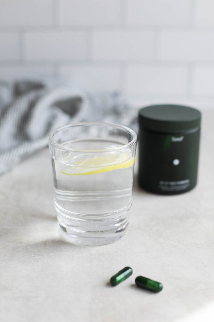 A glass of water with lemon floating int it, Seed probiotics canister in background.