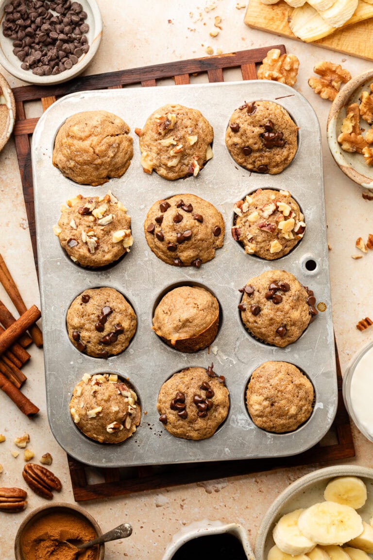 Overhead view of a mini muffin pan filled with banana muffins topped with pecans and chocolate chips.