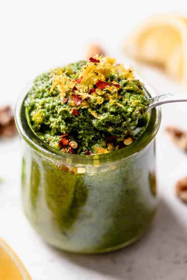 Fresh basil walnut pesto in a small jar topped with lemon zest and red pepper flakes.