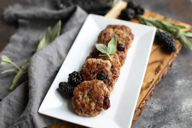 A tray of a row of blackberry sage breakfast sausage topped with fresh sage. 