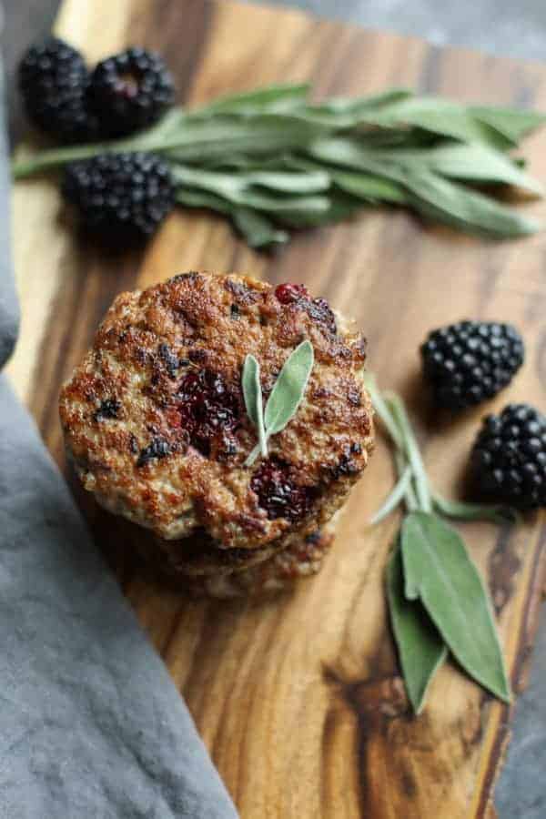 Blackberry Sage Breakfast Sausage on a wood cutting board with berries and sage