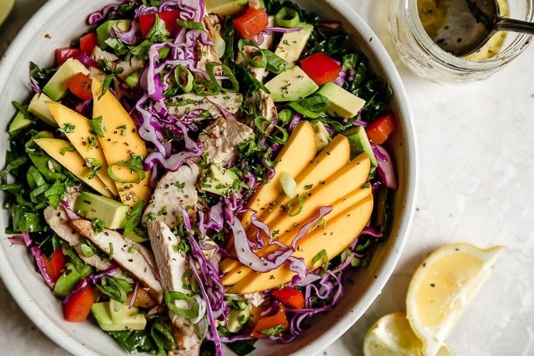 Close up view of a plate of mango chicken salad with avocado topped with shredded chicken, sliced mango, red cabbage, and lemon-lime vinaigrette. 