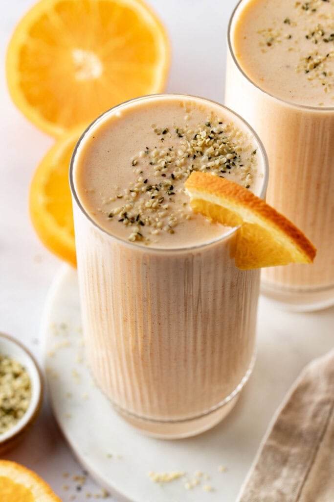 An orange smoothie topped with hem seeds, an orange slice on the rim.