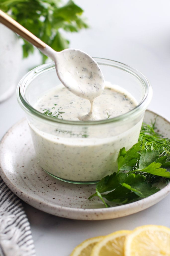 Creamy ranch dressing in a glass bowl with a gold spoon taking a scoop out