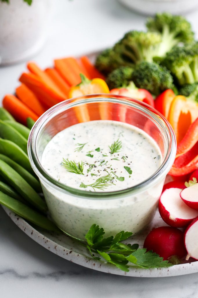 Close up view of creamy Paleo ranch dressing in a small bowl surrounded with freshly cut veggies