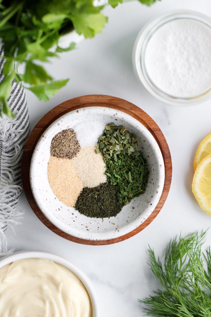 Overhead view of spices for paleo ranch dressing in a small speckled bowl sitting on a wooden coaster.