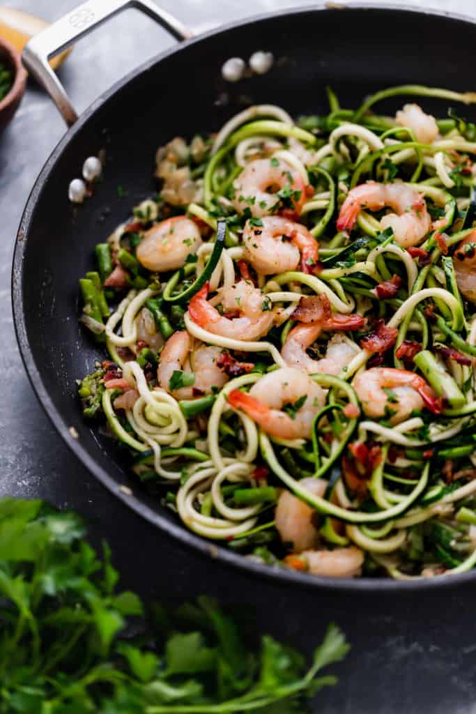 Cast iron skillet with zucchini noodles, asparagus and shrimp with garnish