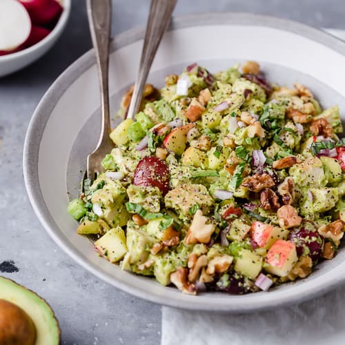 Close up view of a white bowl filled with Avocado Chicken Waldorf Salad and a bowl of radishes on the side