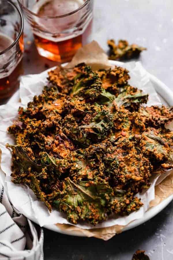 Photo of Cheese Pizza Kale Chips on a plate with two glasses of beer in the background.