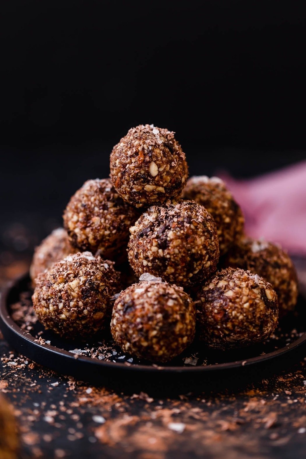 A plate filled with dark chocolate energy bites stacked up and sprinkled with sea salt flakes.