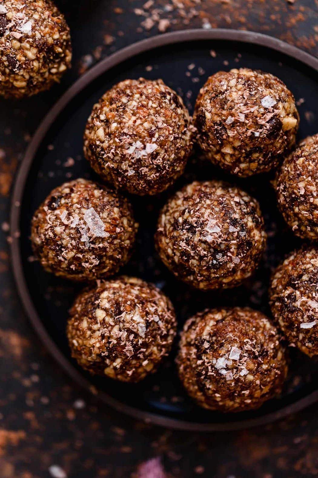 Several cherry chocolate energy bites on a black plate and topped with sea salt flakes