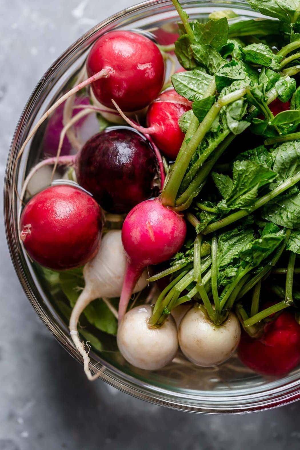 Fresh radishes with greens in a clear bowl filled with water. For the Garlic Roasted Radishes. 