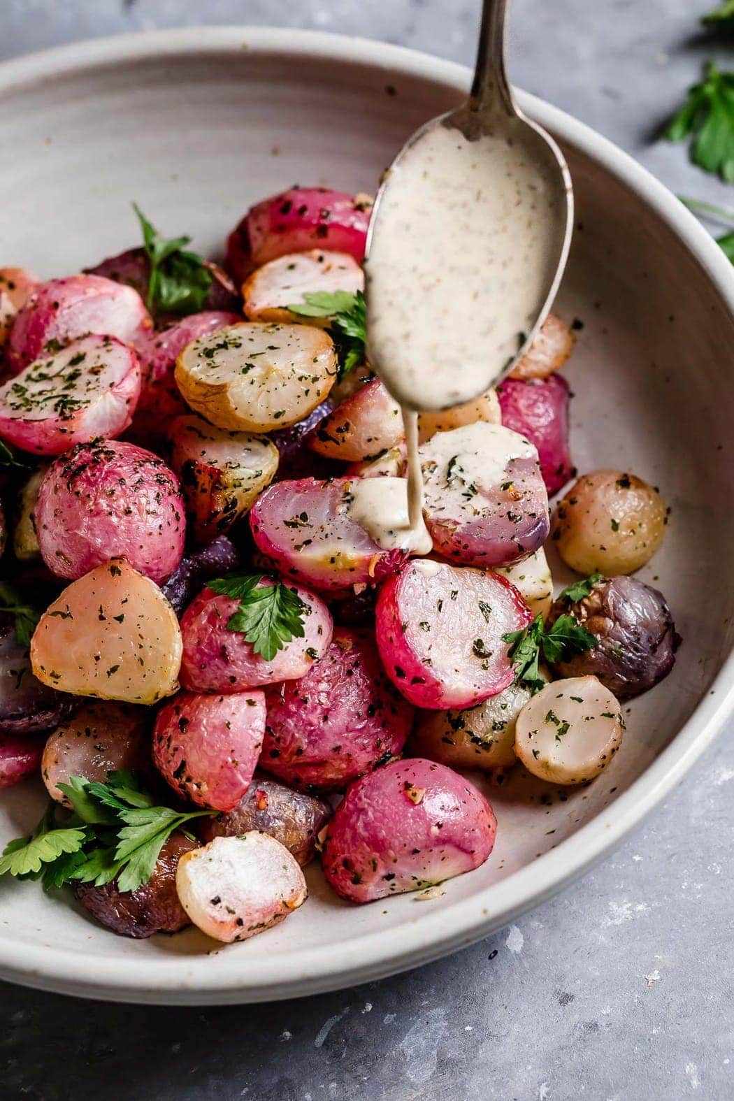 Garlic Roasted Radishes in a serving bowl being drizzled with a ranch. 