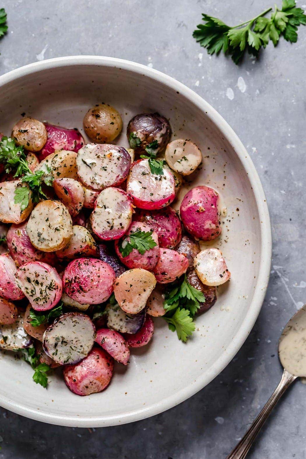 Garlic Roasted Radishes in a serving bowl with ranch drizzled over top. 