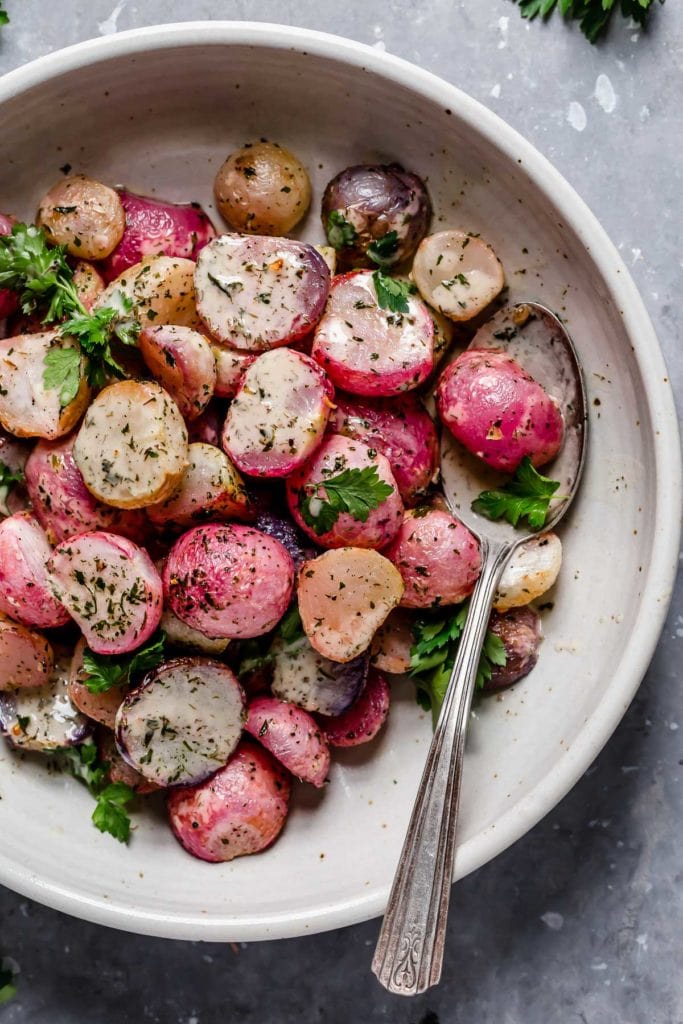 Overhead view of garlic roasted radishes drizzled with ranch dressing in a shallow bowl.