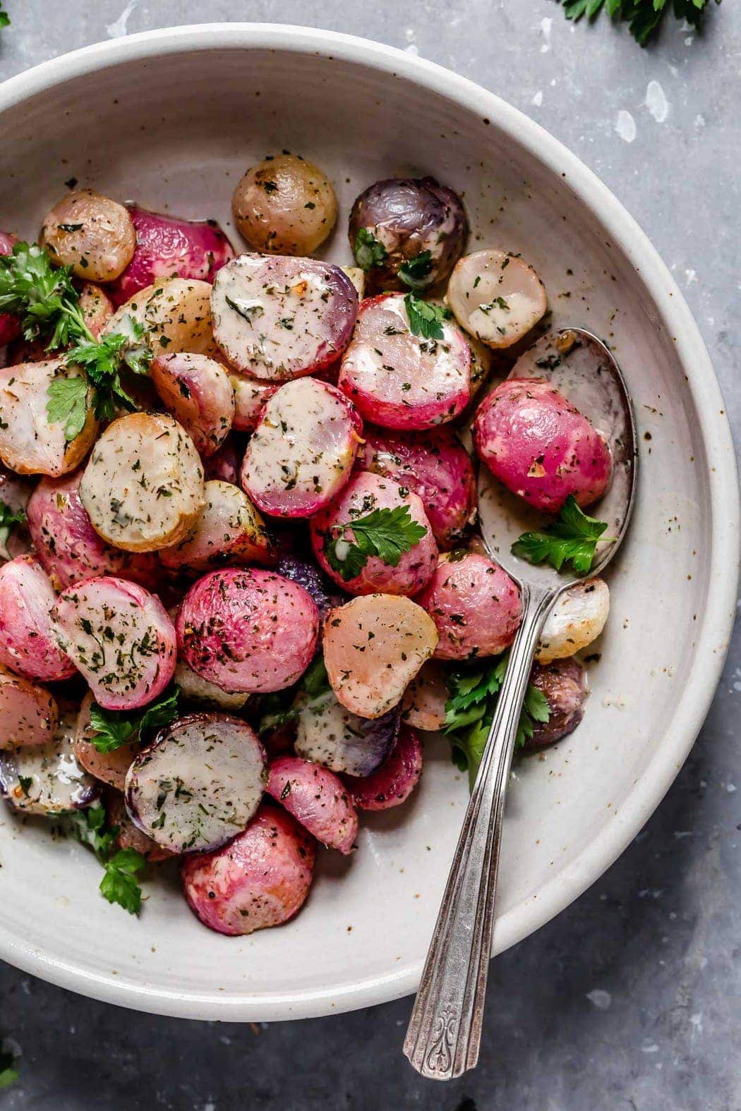 Garlic Roasted Radishes in a cream serving bowl topped with fresh herbs and homemade ranch dressing.