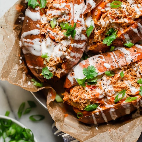 Three buffalo chicken stuffed sweet potatoes in a silver pan topped with ranch dressing and cilantro