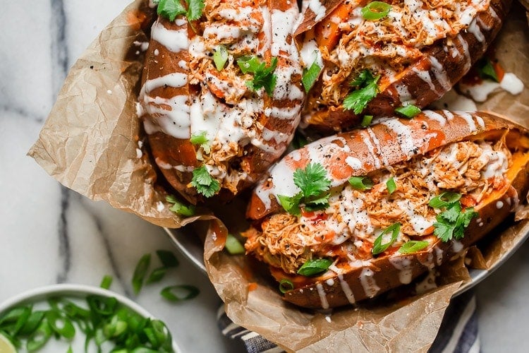Overhead view three baked sweet potatoes stuffed with slow cooker buffalo chicken drizzled with ranch.