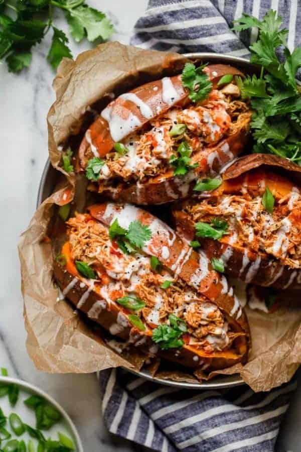 Three Slow Cooker Buffalo Chicken Stuffed Sweet Potatoes drizzled with ranch in a silver pan and garnished with cilantro