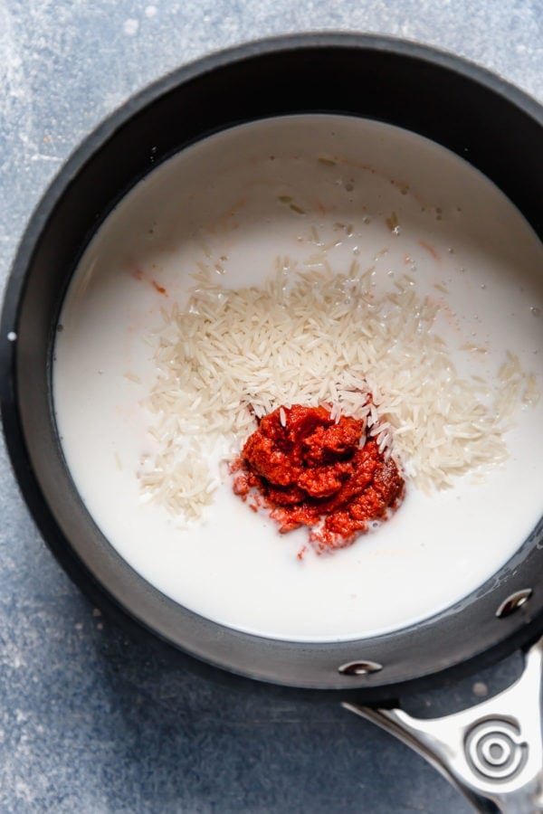A saucepan with coconut milk, uncooked white rice, and red curry paste to make Thai Coconut Curry Rice.