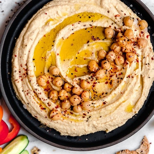 Overhead view black bowl filled with creamy garlic hummus topped with chickpeas, olive oil, and cracked black pepper.