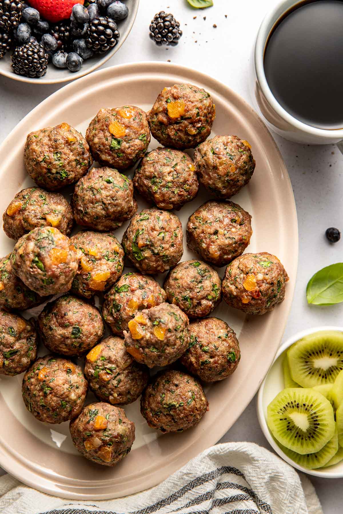 Overhead view of a platter of Apricot Basil Breakfast Meatballs surrounded by a cup of coffee and fresh fruit.
