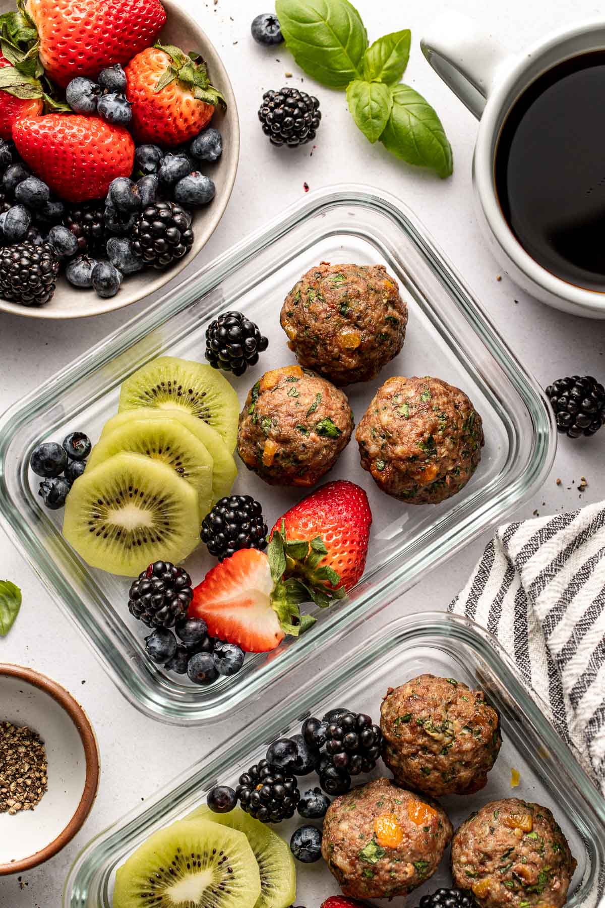 Overhead view of 2 glass meal prep containers filled with fresh fruit and Apricot Basil Breakfast Meatballs. 
