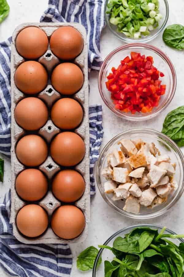 Overhead shot of ingredients for the Buffalo Chicken Egg Muffins including brown eggs, green onion, diced red pepper, diced chicken and spinach. 