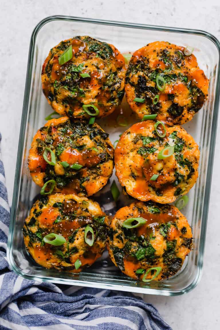 A glass container of buffalo chicken egg muffins topped with buffalo sauce and green onions.