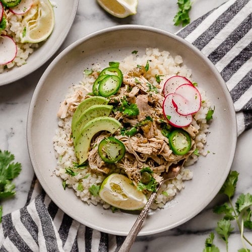 Shredded easy salsa verde chicken over cauliflower rice, topped with radishes, avocado, cilantro, and cracked black pepper