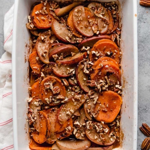 Overhead view cinnamon sweet potato apple bake topped with chopped pecans in white baking dish