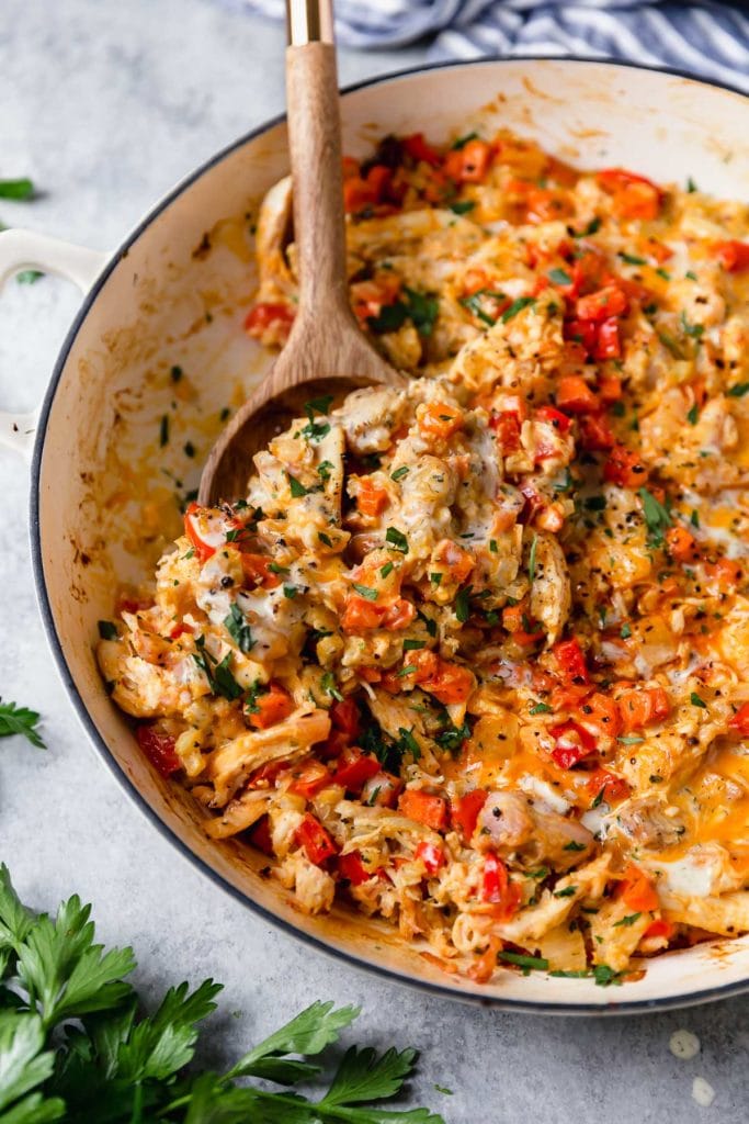 Serving of Creamy buffalo chicken veggie casserole in a white skillet being scooped up with wooden spoon.