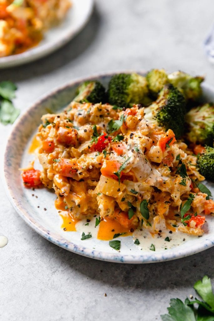 Close up view serving of creamy buffalo chicken casserole on plate with roasted broccoli