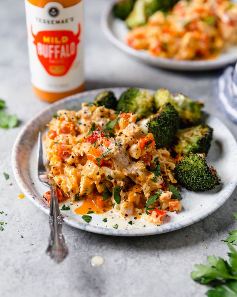 Side view serving of creamy buffalo chicken casserole with roasted broccoli on blue and white plate