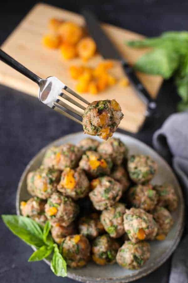 Apricot-Basil Breakfast Meatballs in a white bowl with one on a fork moving towards the camera