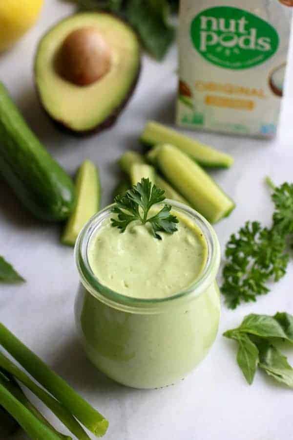 Green Goddess Dressing in a glass jar with ingredients on a white table